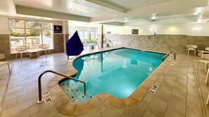 An indoor swimming pool with a pool lift, tiled flooring, and a view of the outside through large windows.