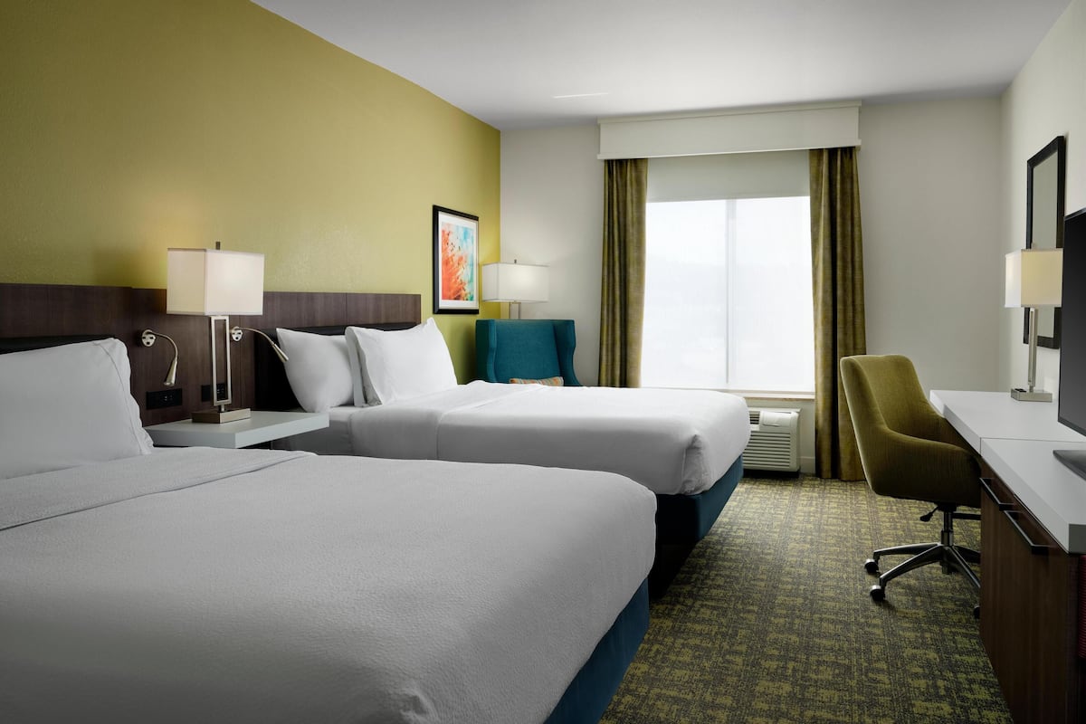 A hotel room with two beds, a desk, a chair, a TV, and a window with curtains.