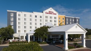 A Hilton Garden Inn hotel with a central entrance, outdoor seating, and a parking lot.