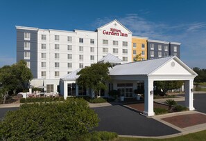 A Hilton Garden Inn hotel with a central entrance, outdoor seating, and a parking lot.