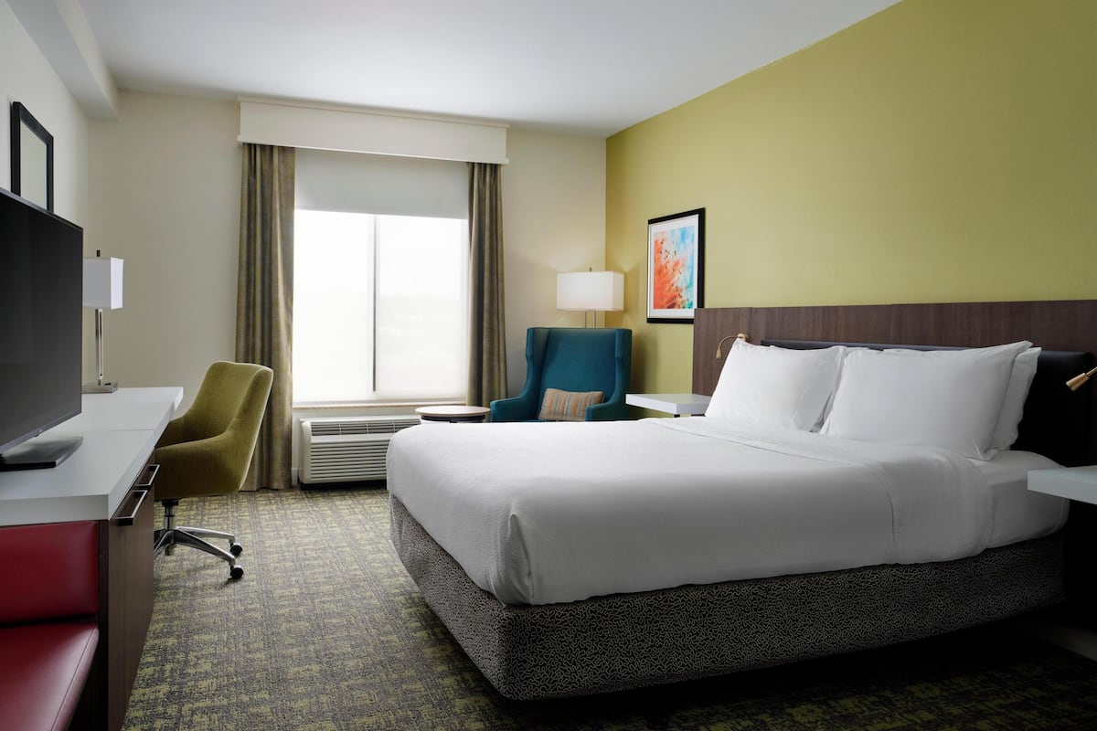 A hotel room with a large bed, a desk with a TV, a chair, a lamp, and a window with curtains.