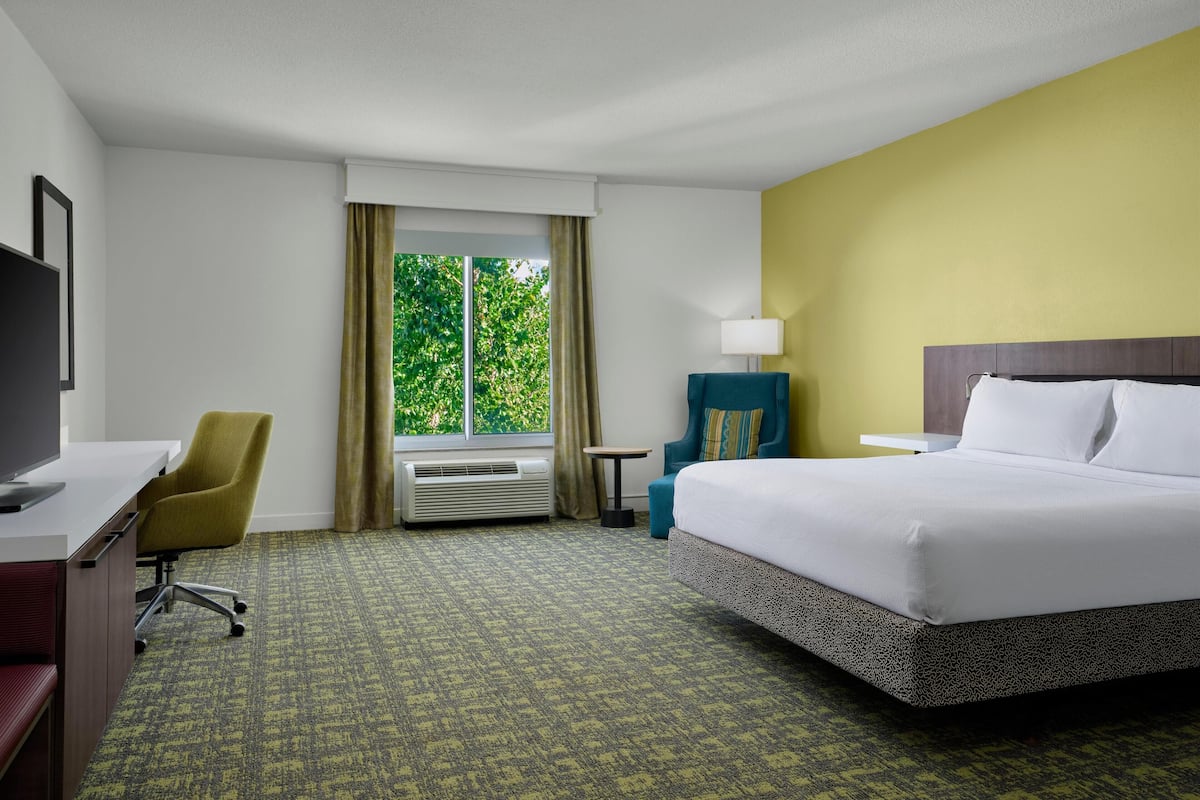 A hotel room with a bed, desk, chair, and a window with curtains.