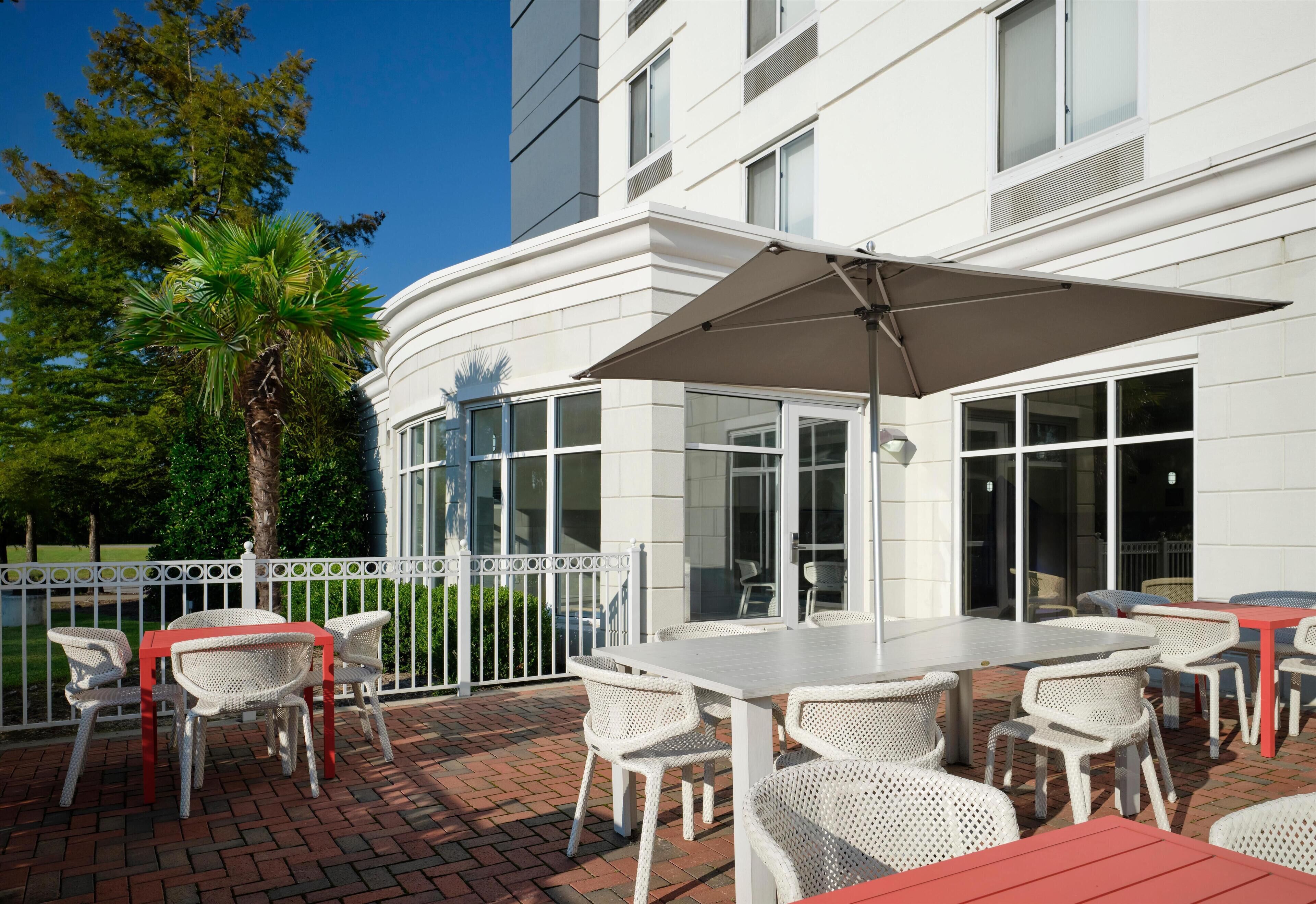 An outdoor patio with white wicker furniture and a large umbrella.