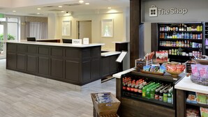 A hotel reception area with a counter, a shop, and a display of beverages. - Hilton Garden Inn Greensboro (Greensboro)