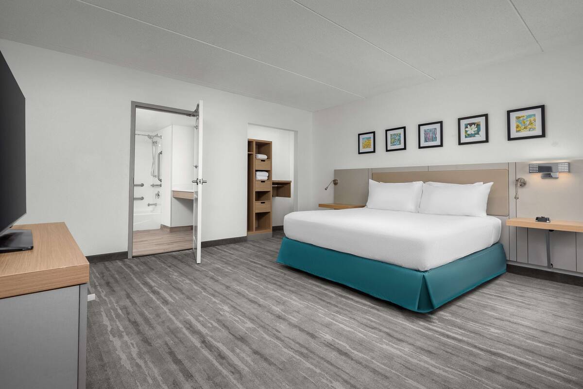 A hotel room with a bed, a desk, a TV, a shower, and a bathroom.