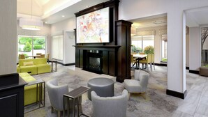 A modern living room with a fireplace, comfortable seating, and a large TV screen. - Hilton Garden Inn Greensboro (Greensboro)