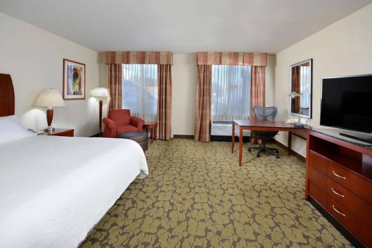 A hotel room with a bed, desk, TV, and two chairs.