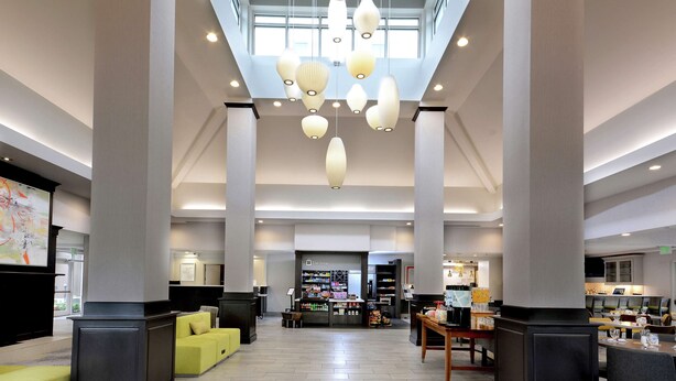 A spacious lobby with high ceilings, modern pendant lighting, and a central seating area. - Hilton Garden Inn Greensboro (Greensboro)