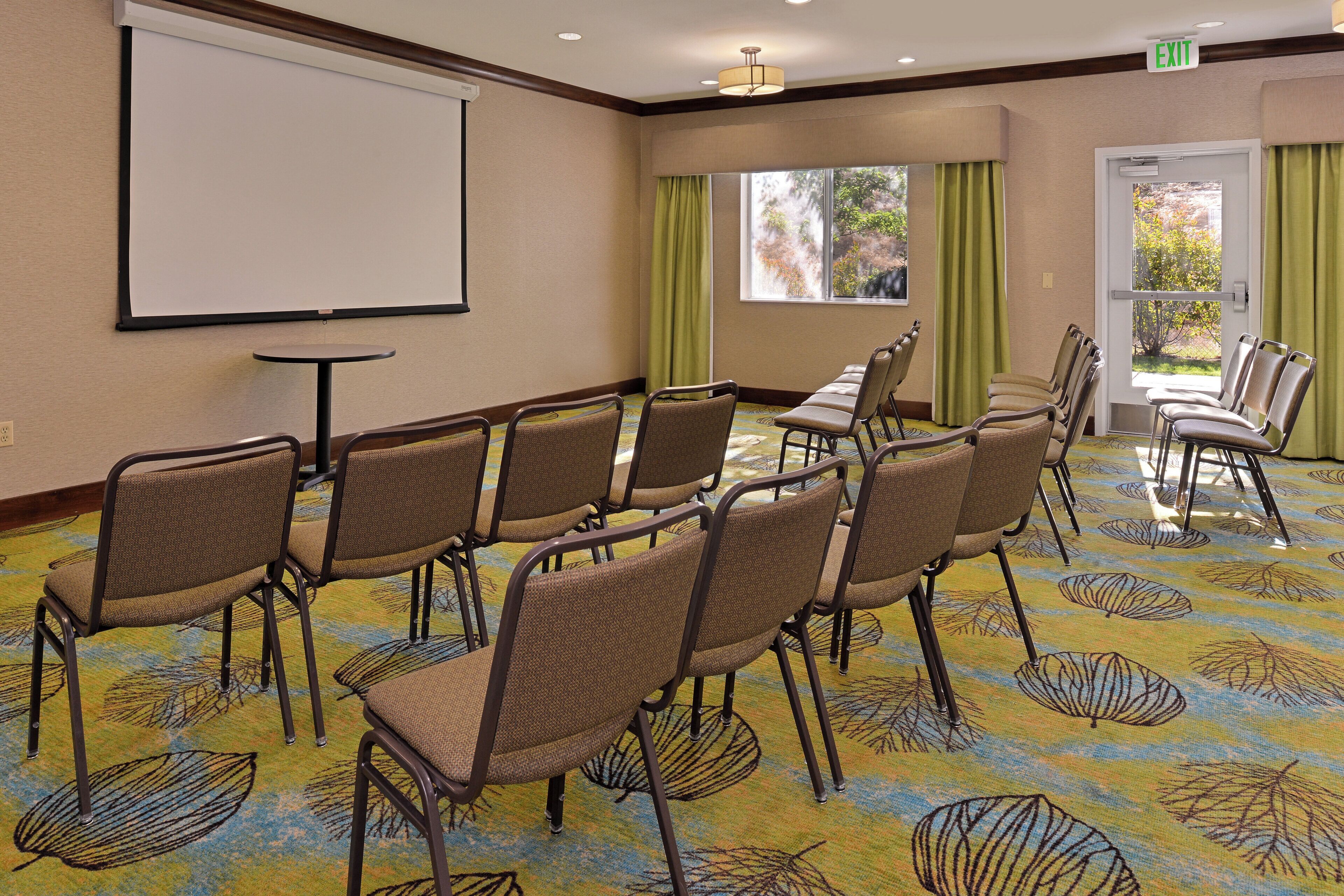 Uma sala de conferências com tela de projeção, mesa e cadeiras dispostas para uma reunião.