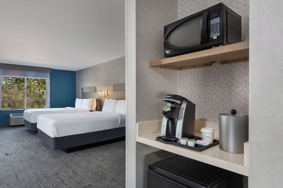 A hotel room with two beds, a coffee machine, a microwave, and a trash bin.