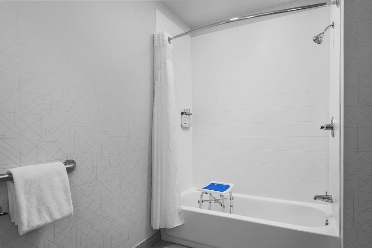 A modern bathroom with a walk-in shower, a bathtub with a blue seat, and a towel rack.