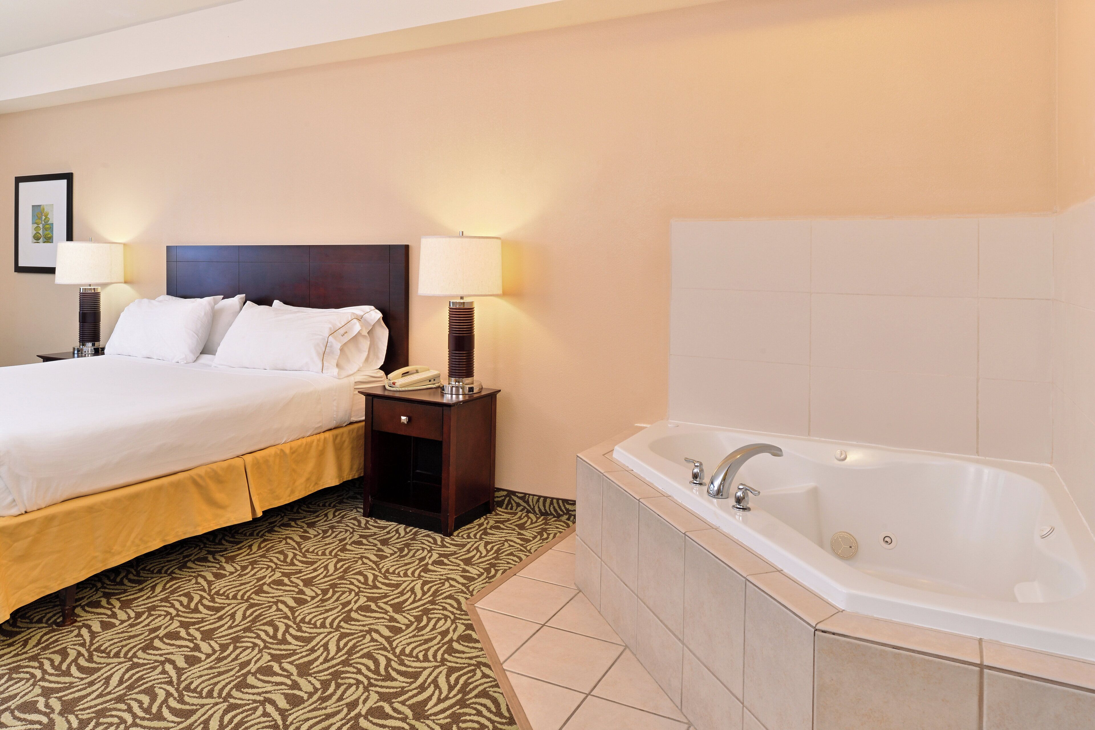 A hotel room with a bed, bedside lamps, a telephone, a nightstand, and a bathtub.