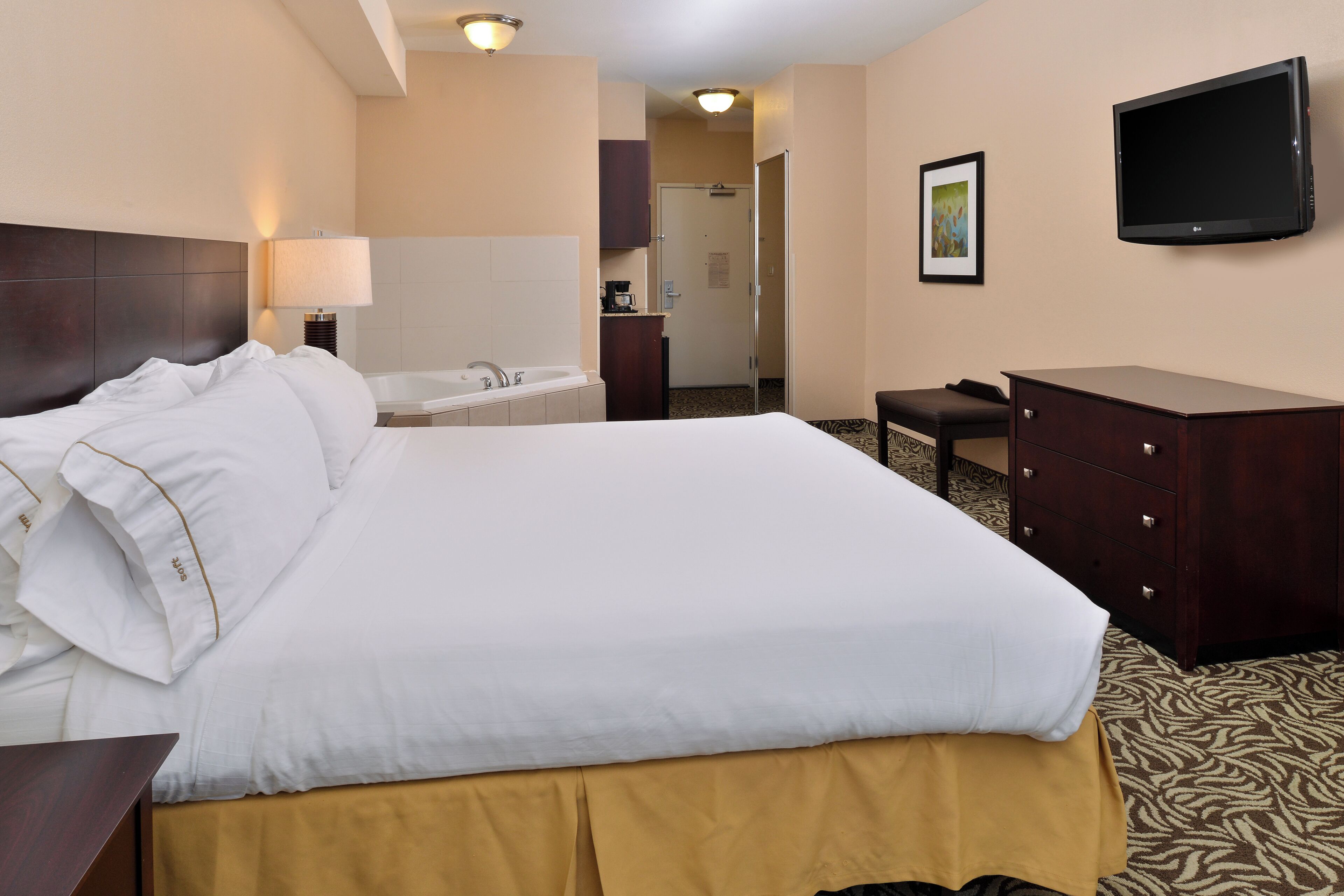 A hotel room with a large bed, a desk, a flat-screen TV, and a bathroom visible in the background.