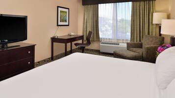 Une chambre d’hôtel avec un grand lit, un bureau avec un téléphone, une chaise, une télévision et une fenêtre avec des rideaux.