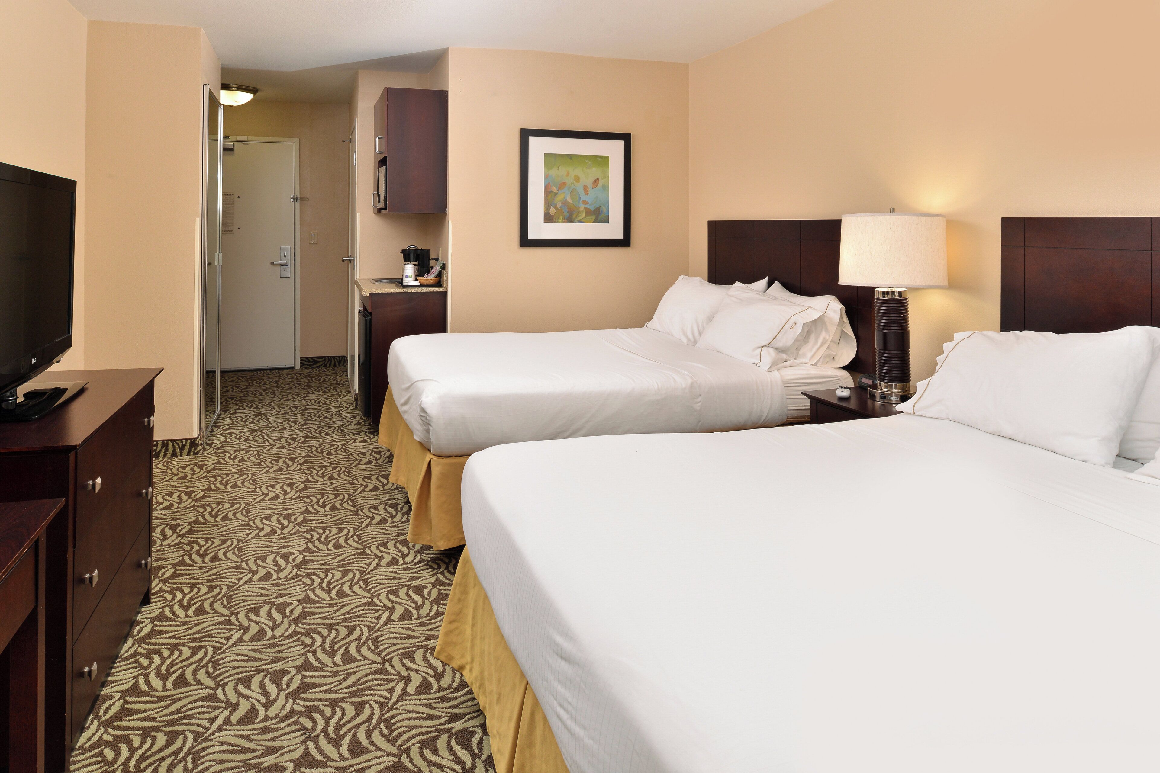 A hotel room with two beds, a television, a coffee maker, and a framed picture on the wall.