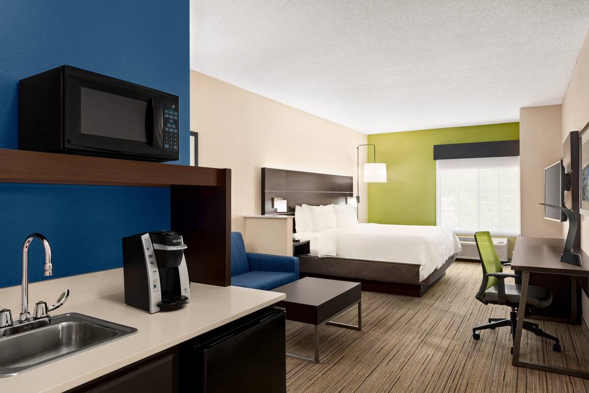 A hotel room with a kitchenette, a bed, a desk, a chair, and a TV.