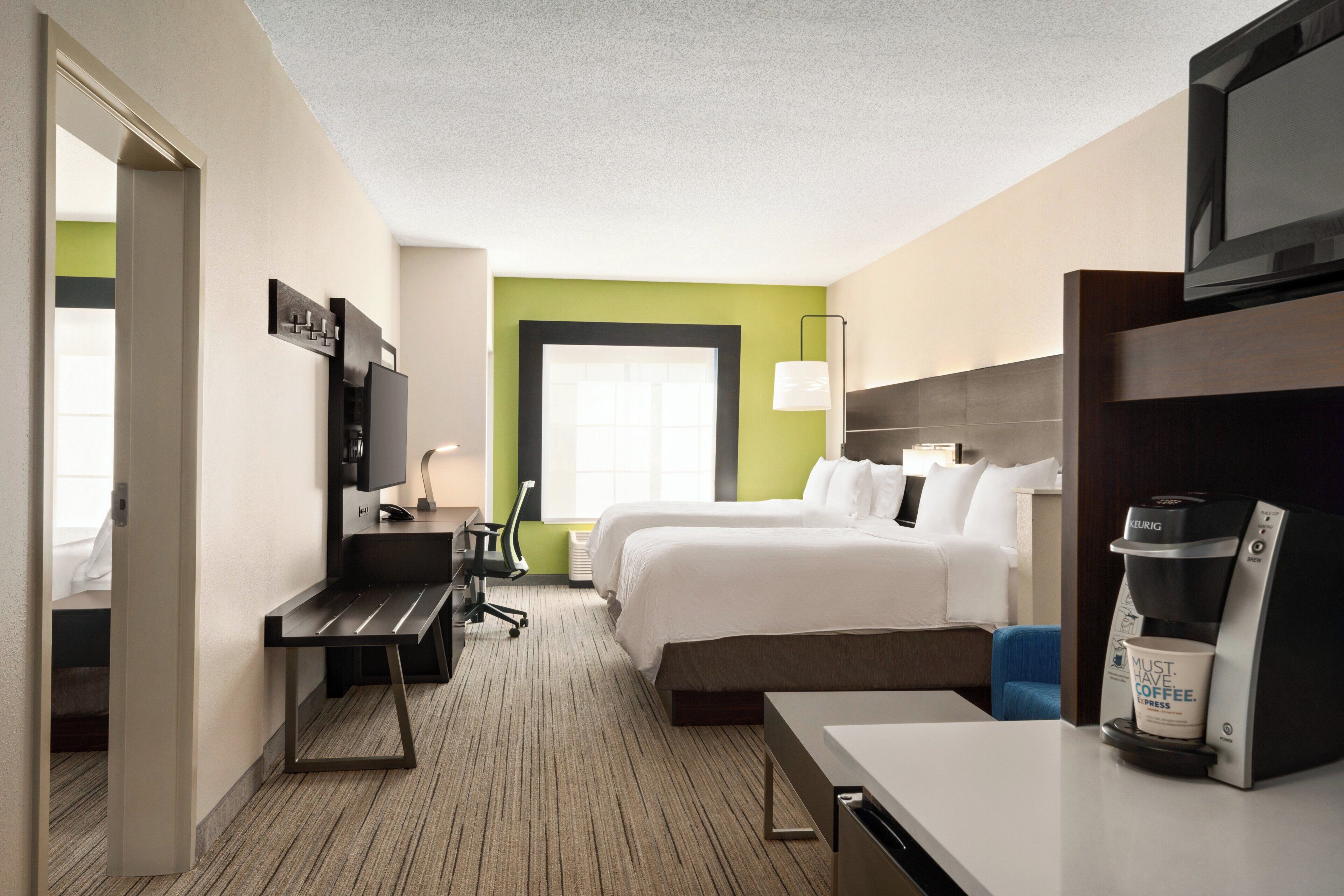 Habitación de hotel con cama, escritorio, silla, cafetera y televisión.