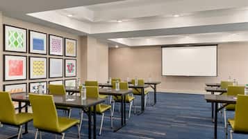 A conference room with tables and chairs, a projector screen, and framed artwork on the wall.