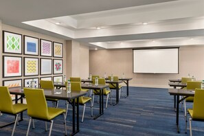 A conference room with tables and chairs, a projector screen, and framed artwork on the wall. - Holiday Inn Express & Suites McAlester by IHG (McAlester)