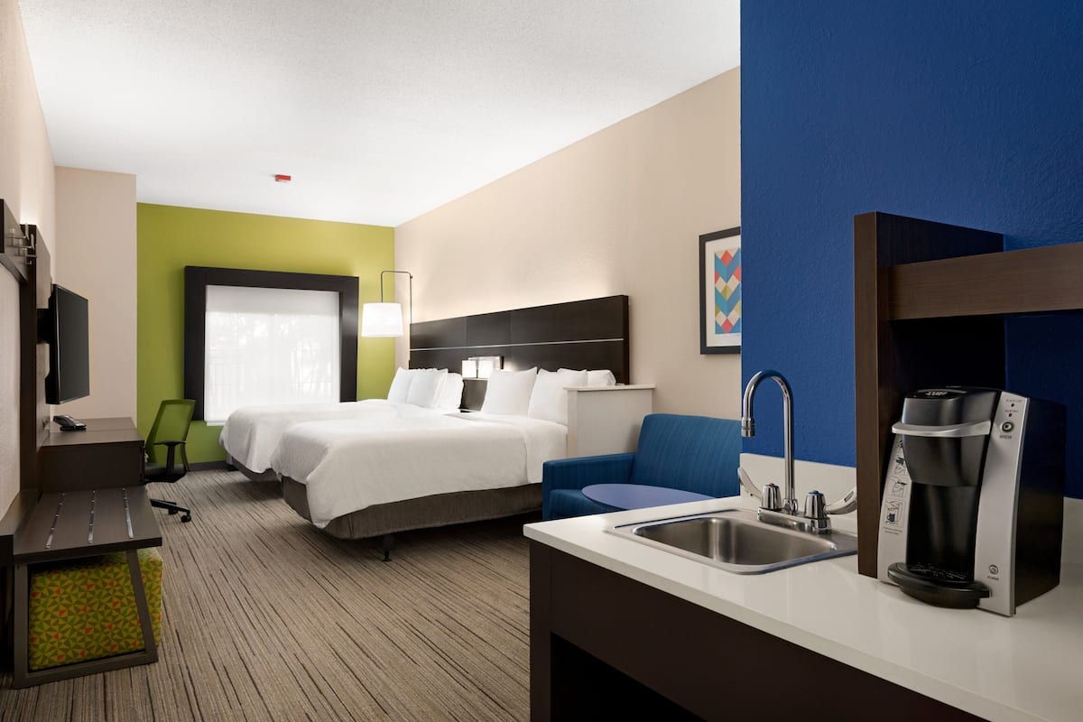 A hotel room with a bed, a desk with a coffee maker, a chair, a TV, and a window.