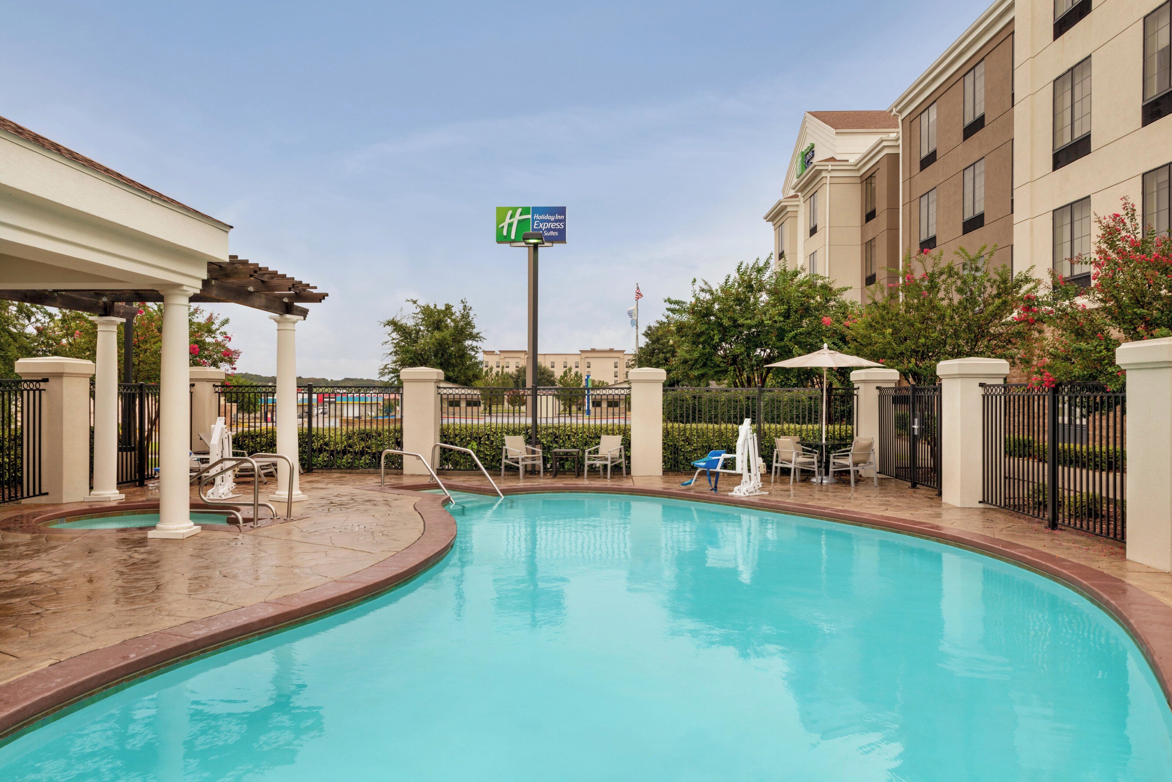 A hotel pool area with a clear sky, a Holiday Inn Express sign, and a building in the background.