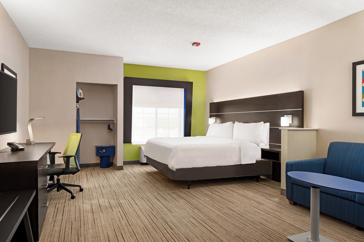 A hotel room with a bed, a desk, a chair, a TV, a window, and a couch.