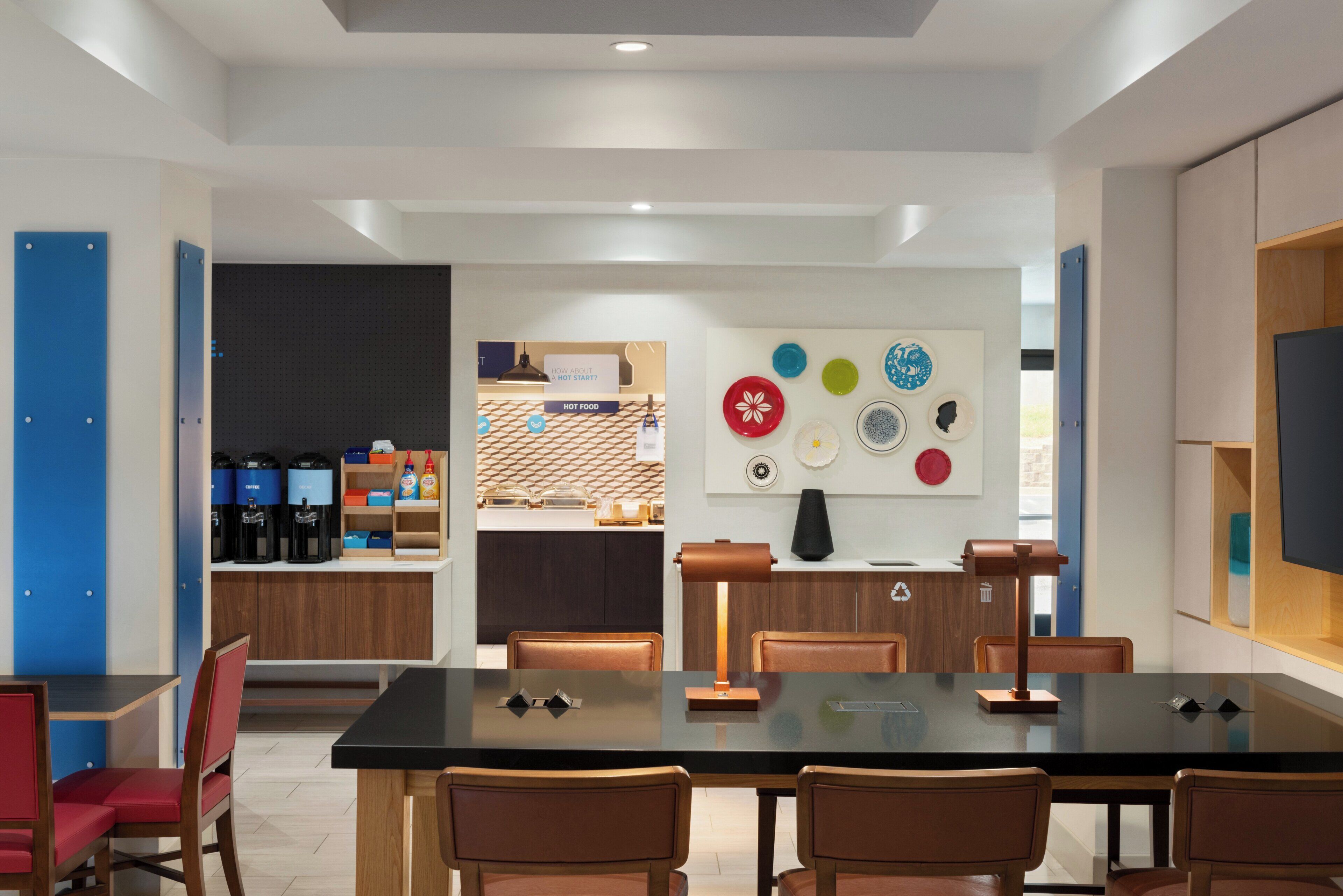A modern dining area with a long table, chairs, a coffee station, and a counter with a menu.