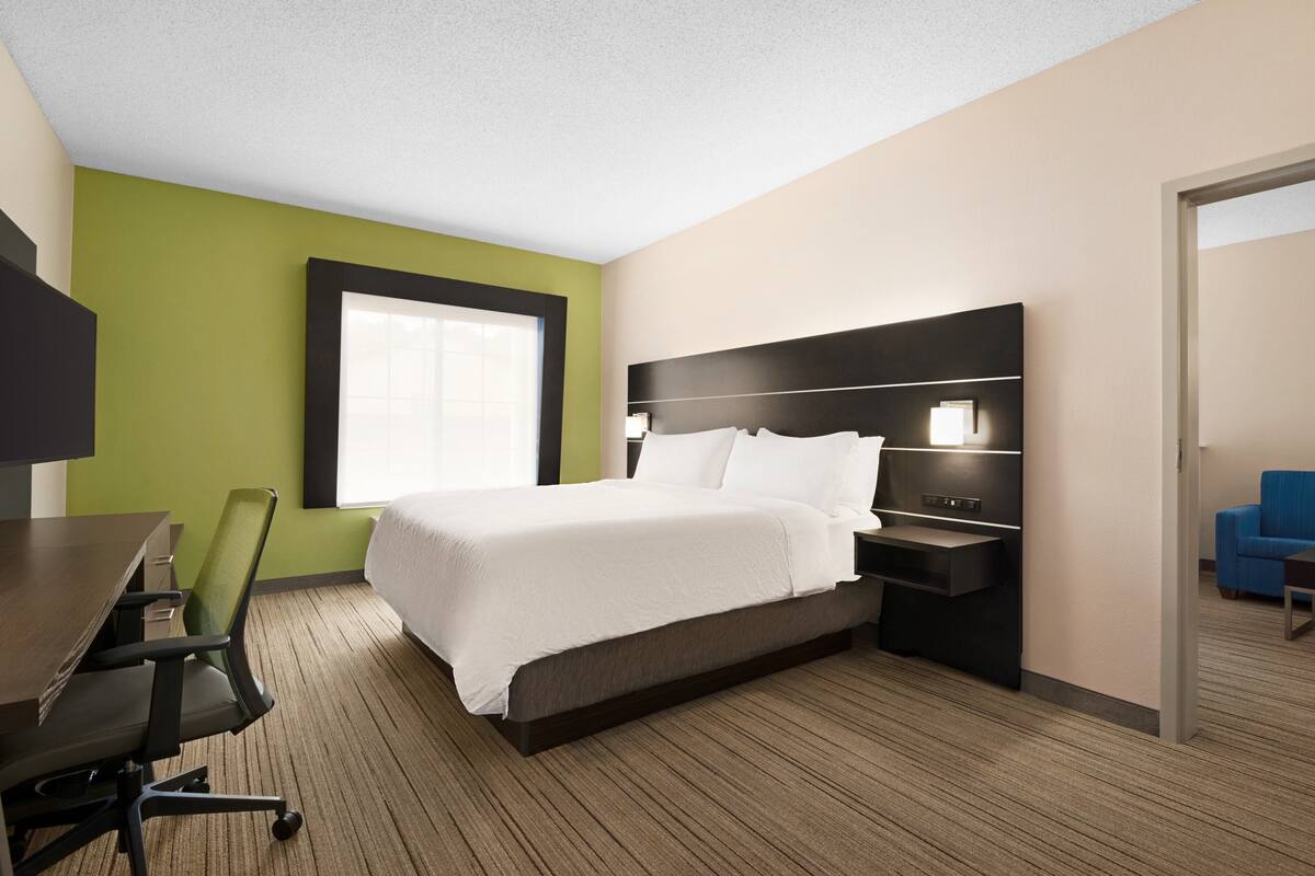A hotel room with a bed, a desk, a chair, a nightstand, and a window.