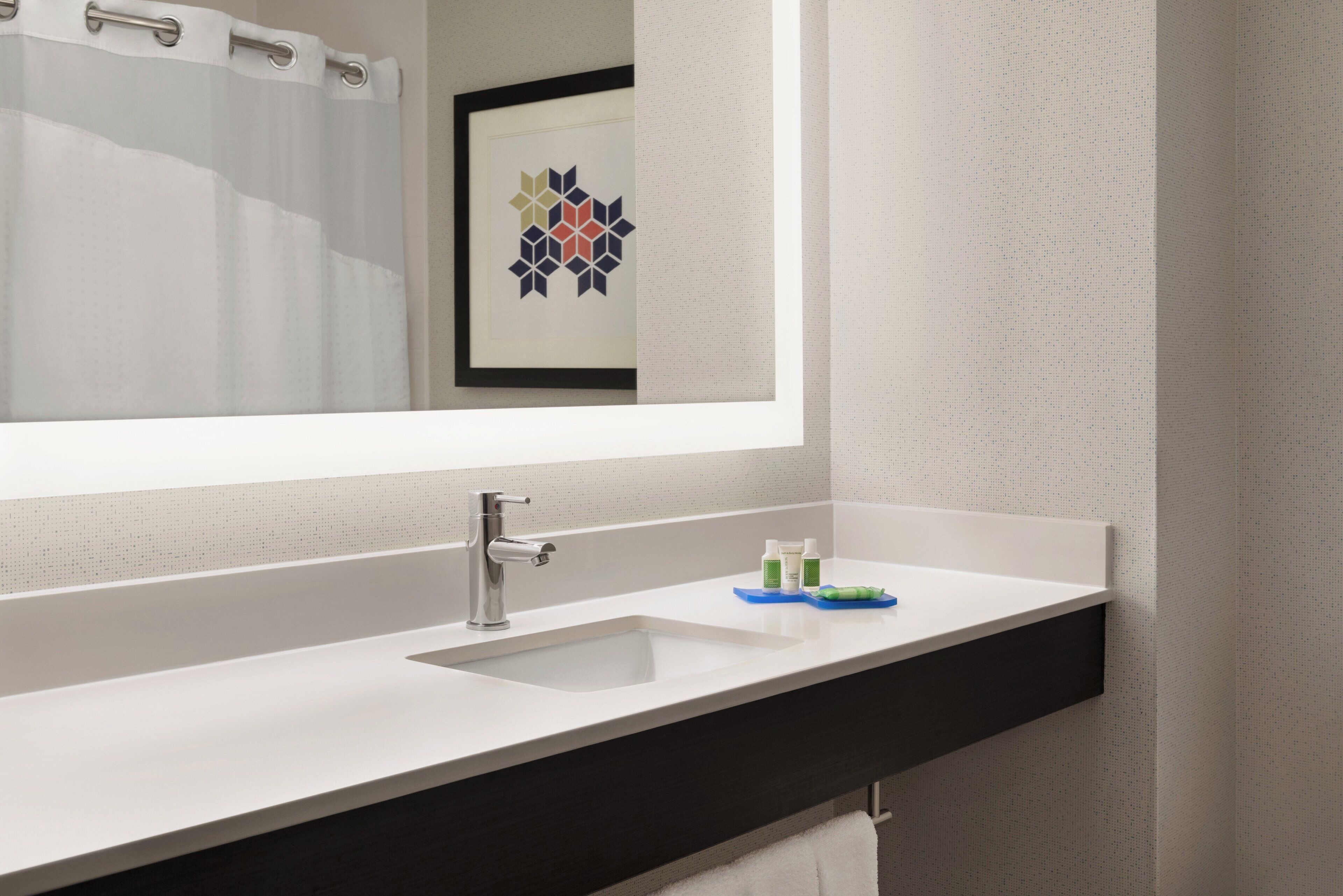 A bathroom with a white sink, a mirror, and a framed artwork above the mirror.
