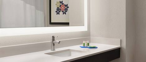A bathroom with a white sink, a mirror, and a framed artwork above the mirror.