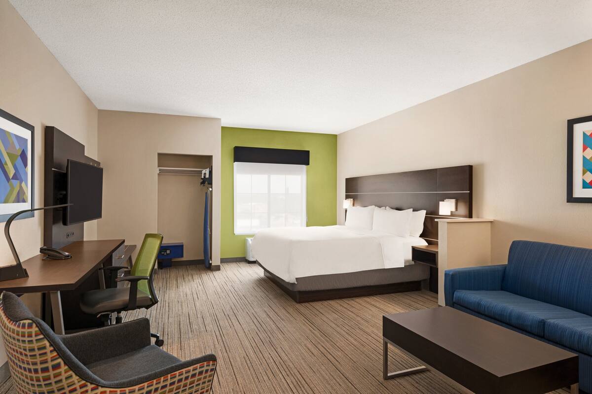 A hotel room with a bed, a desk with a computer, a chair, a sofa, and a television.