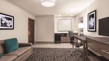 A hotel room with a sofa, a desk, a chair, a TV, and framed pictures on the walls.