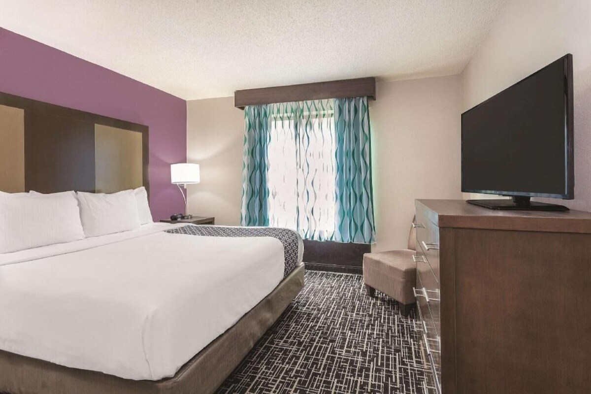 Une chambre d’hôtel avec un lit, une télévision, un bureau et une fenêtre avec des rideaux.