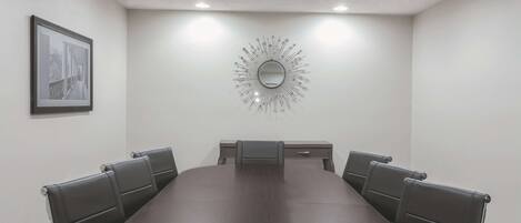 A conference room with a long table, six chairs, a small desk, a framed picture on the wall, and a decorative mirror.