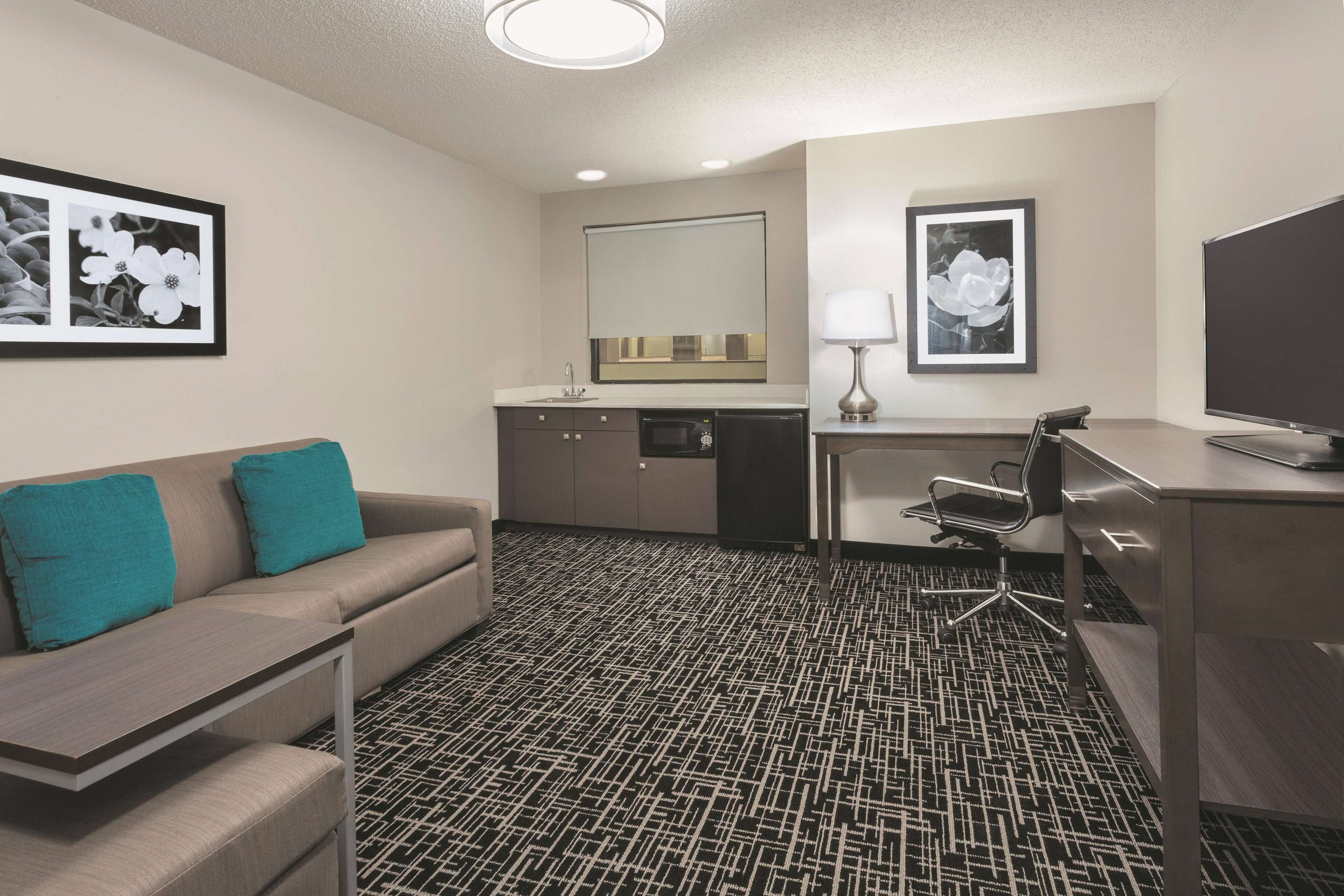 A hotel room with a sofa, a desk, a chair, a TV, a lamp, a mirror, and framed pictures on the walls.