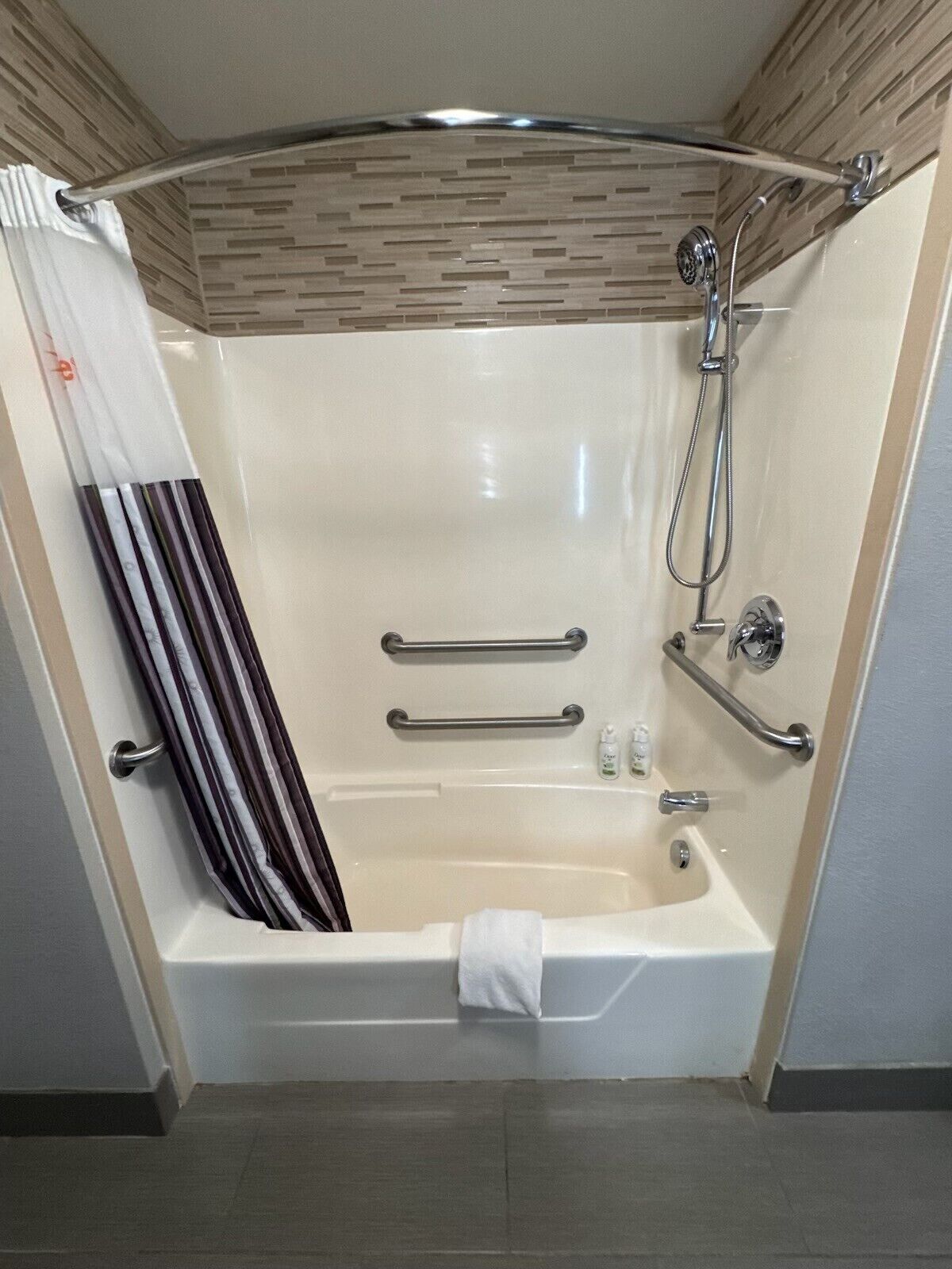 A modern bathroom with a bathtub, grab bars, a showerhead, and a towel rack.