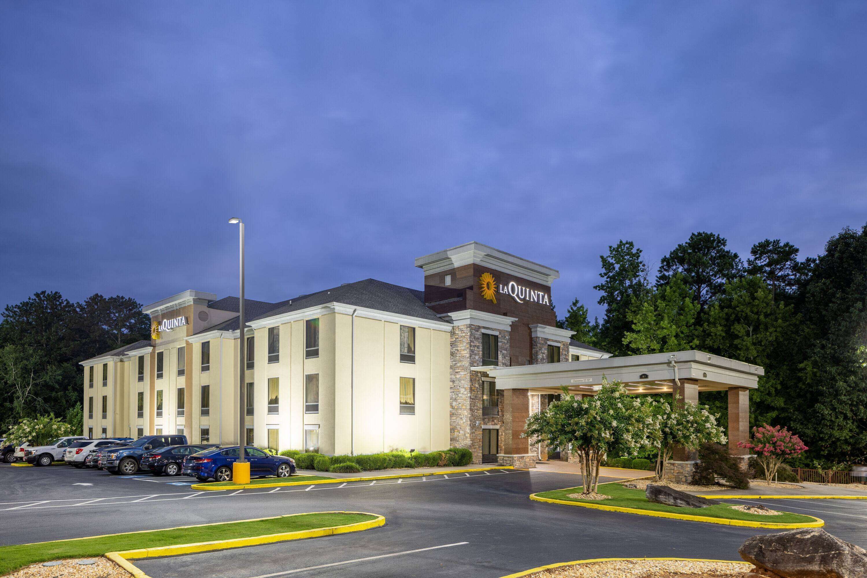 A hotel with a central entrance, multiple parking spaces, and a landscaped area with trees and shrubs.
