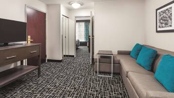 A hotel room with a black and white patterned floor, a sofa with teal cushions, a TV on a wooden stand, and a framed picture on the wall.