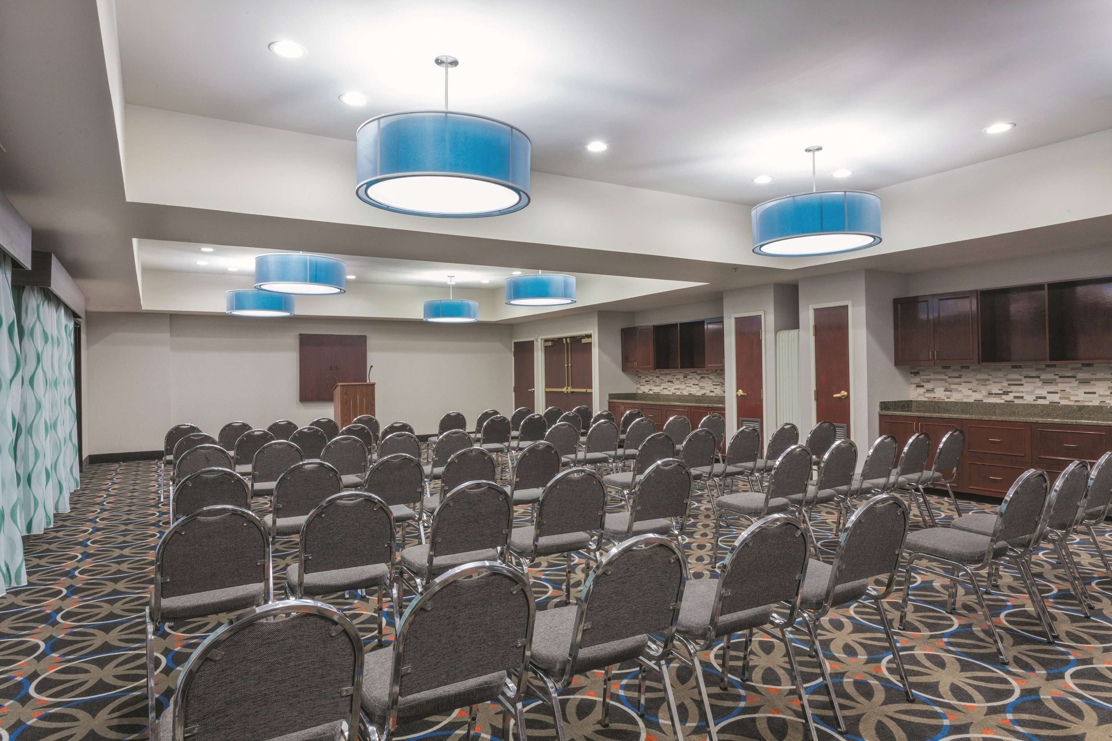 A conference room with rows of chairs, blue pendant lights, and a patterned carpet.
