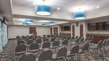A conference room with rows of chairs, blue pendant lights, and a patterned carpet.