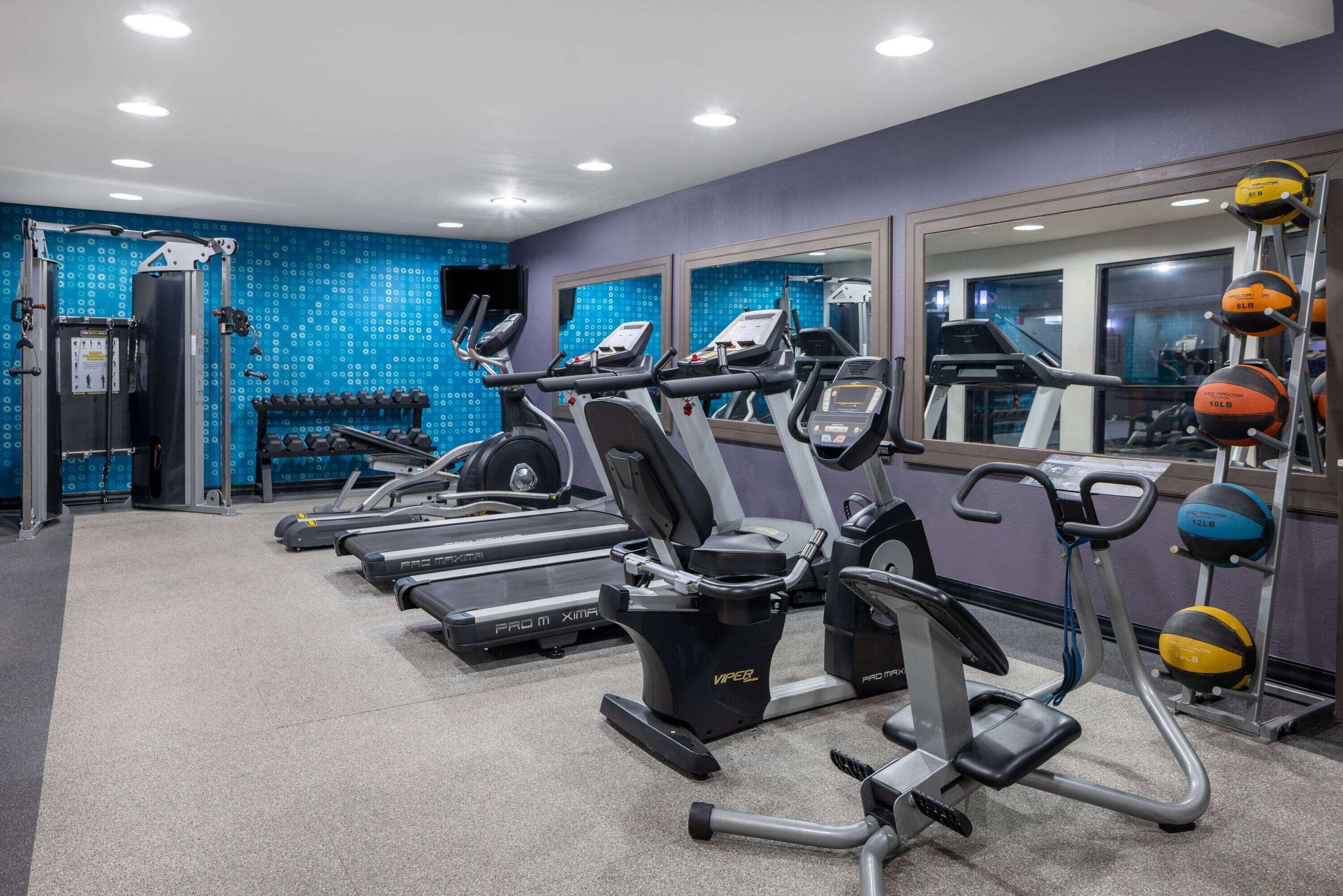 A gym with treadmills, ellipticals, and a mirrored wall.