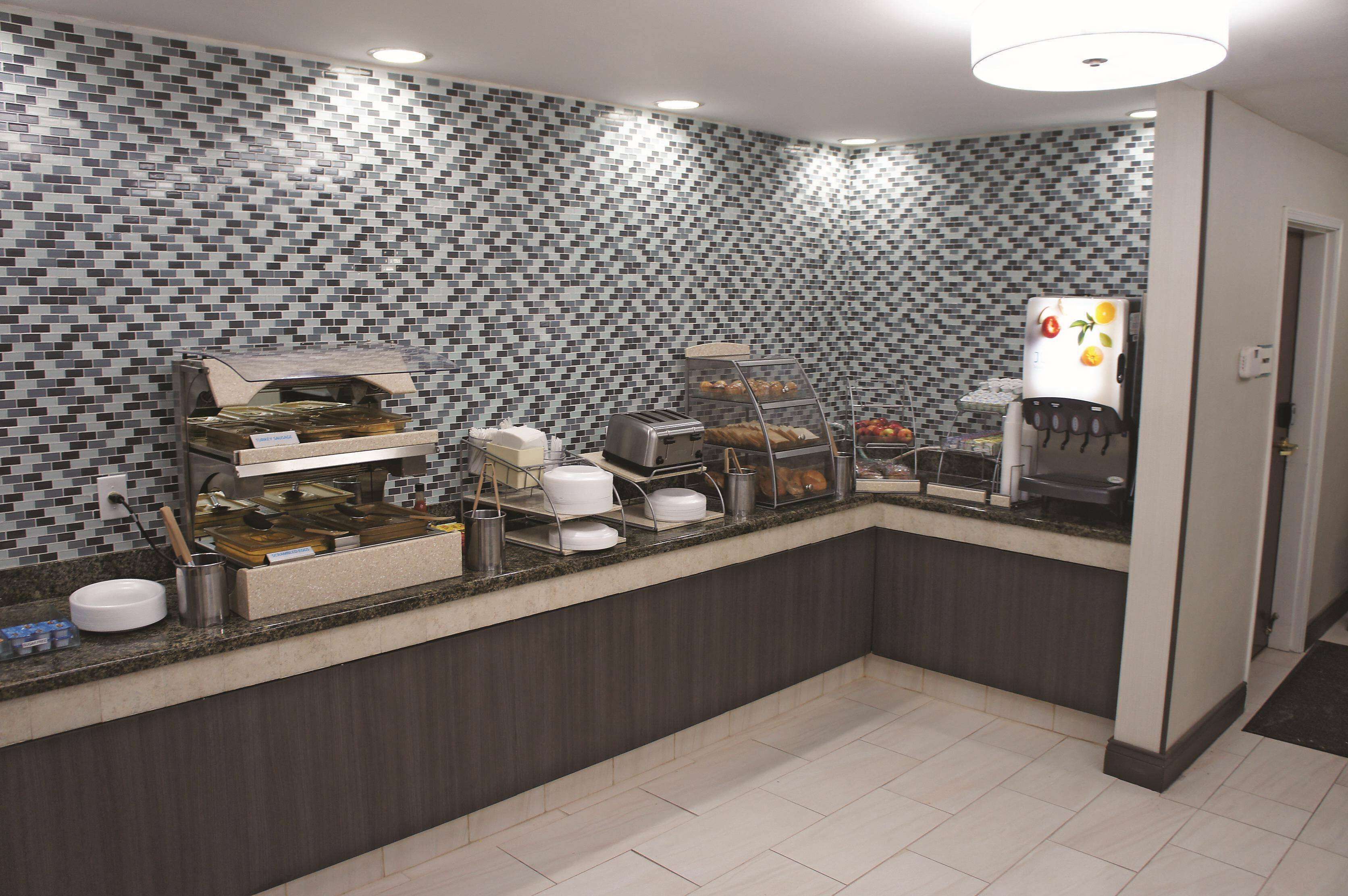 A breakfast bar with a tiled backsplash, a coffee machine, and a refrigerator with fruit magnets.