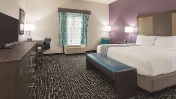 A hotel room with a bed, a desk with a chair, a television, and a window with curtains.