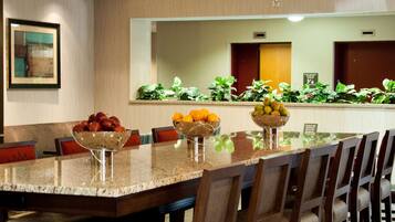A hotel dining area with a long table, multiple chairs, a chandelier, and a fruit bowl on the table.