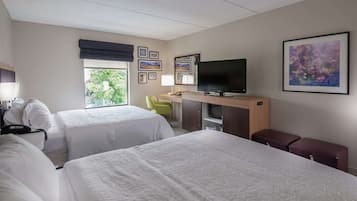 A hotel room with two beds, a desk with a TV, a chair, and a window with a view of trees.
