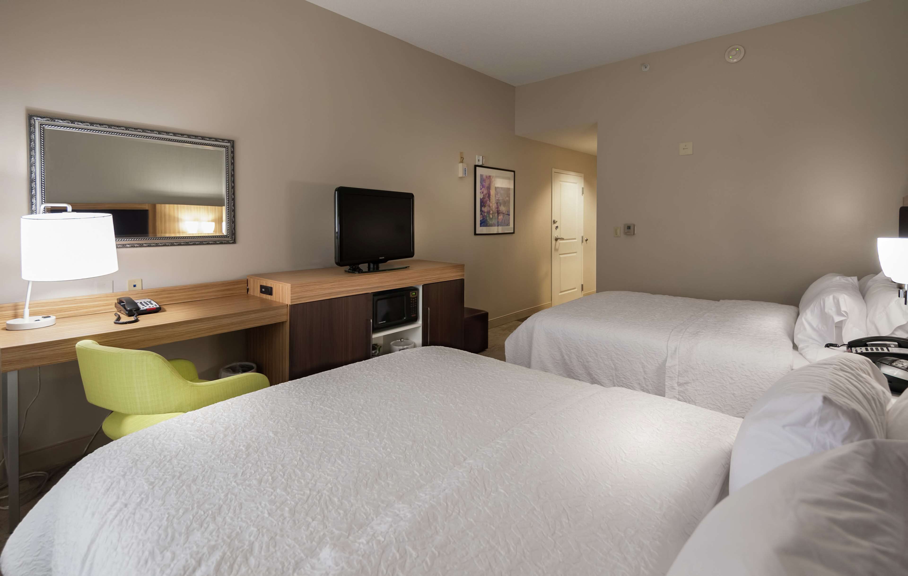 Habitación de hotel con dos camas, un escritorio, televisión, una lámpara y una silla.