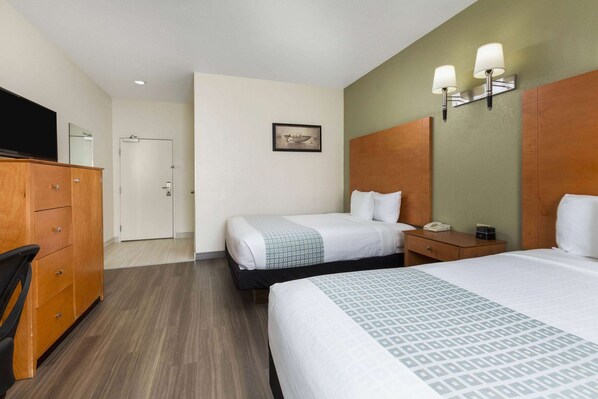 A hotel room with two beds, a wooden dresser, a desk with a telephone, and a wall-mounted light fixture.