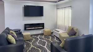 A modern living room with a flat-screen TV mounted on the wall, a fireplace, and a sofa set. - La Quinta Inn & Suites by Wyndham Tulare (Tulare)