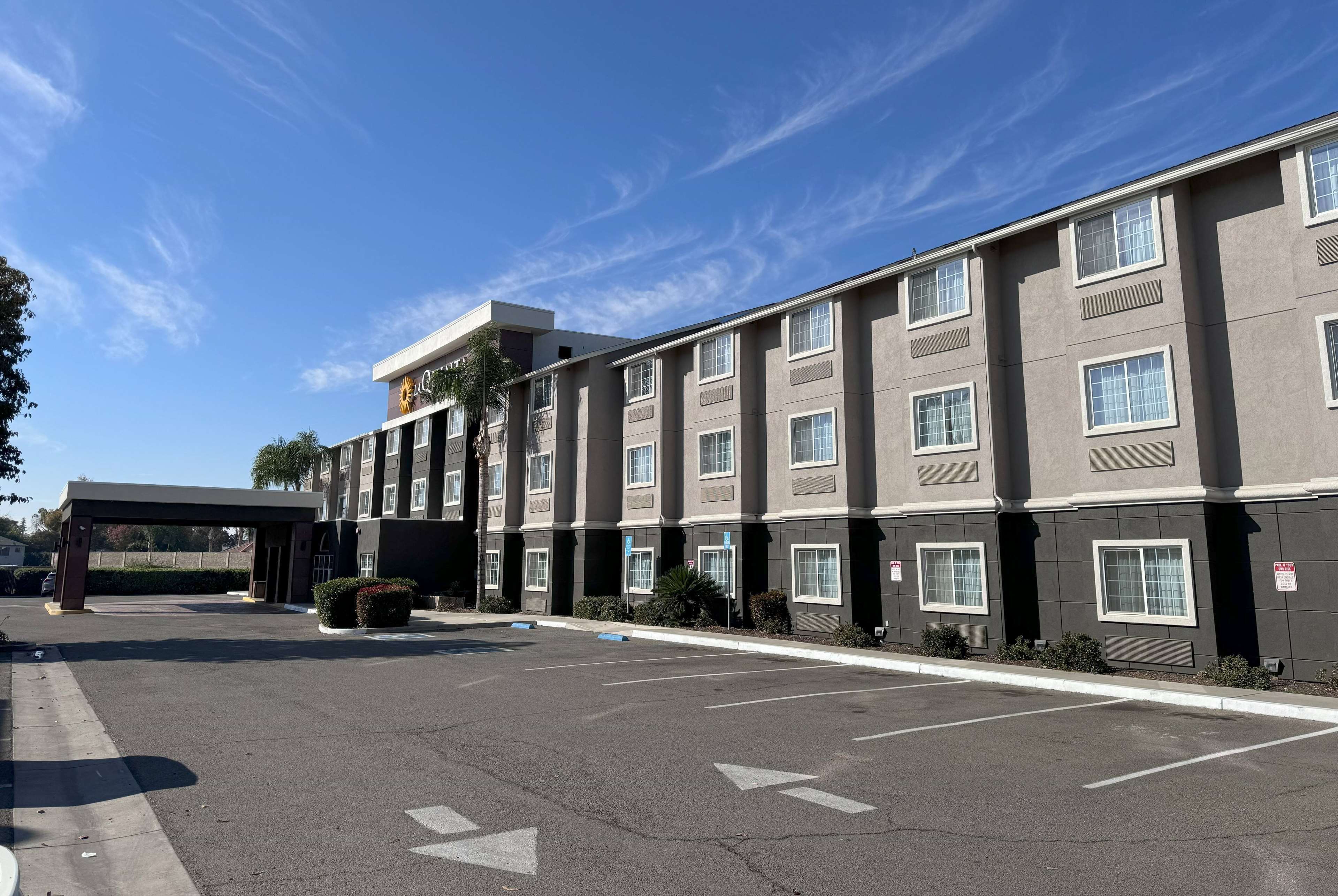 A multi-story hotel with a covered entrance, a parking lot, and a clear blue sky.