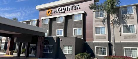 Un hotel con un llamativo letrero de 'La Quinta', que presenta un logo de sol. Exhibe un estilo arquitectónico moderno con techo plano y múltiples ventanas.